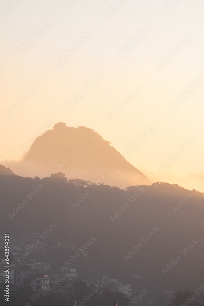 Rio de Janeiro, Brazil: city skyline with the Sugarloaf Mountain and Cable Car shrouded in fog after the dawn in the early morning sunlight seen from an high terrace on Copacabana beach