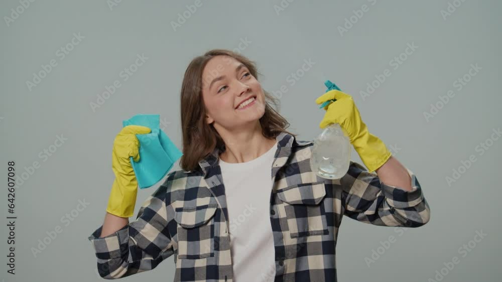 A Portrait of a Smiling Young Woman in Yellow Gloves,Holding a Cleaning Spray Bottle and Rag, Dancing on the Gray Background.A Female Housewife is Preparing to Clean. Speed Cleaning. A Portrait of a Smiling Young Woman in Yellow Gloves,Holding a Cleaning Spray Bottle and Rag, Dancing on the Gray Background.A Female Housewife is Preparing to Clean. Speed Cleaning.