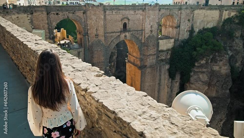 A girl tourist walking by the New Bridge Interpretation Center in Ronda, Spain. A female exploring looking at the Centro de Interpretación del Puente Nuevo with a huge medieval arch bridge