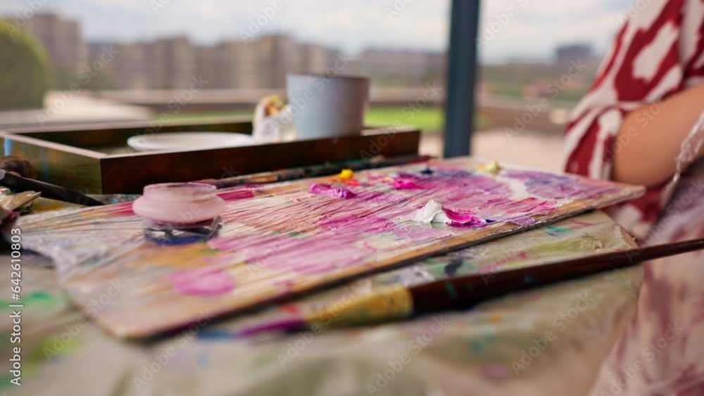 A close-up of a girl artist sitting near an easel and taking paint from ...