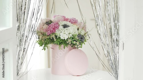 An elegant bouquet of fresh roses, peonies, and daisies in a pink box, beautifully arranged and placed by a light-filled window.