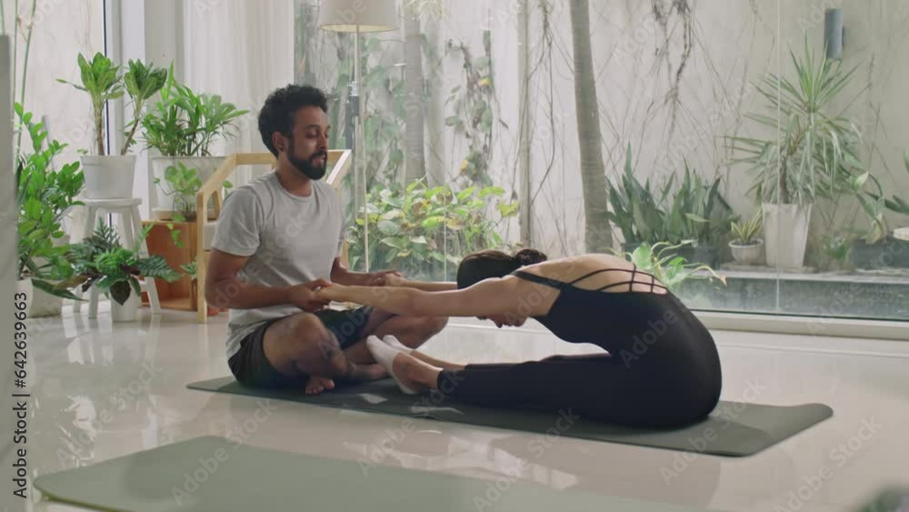 Fitness trainer helping young woman with doing forward fold stretch during personal workout at home Fitness trainer helping young woman with doing forward fold stretch during personal workout at home