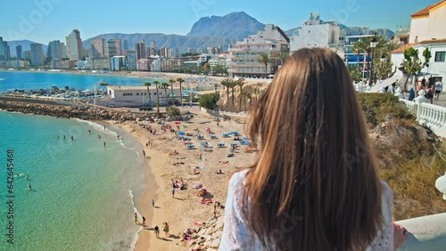 A beautiful girl in a dress looking at a scenic view of Spanish Beach and the Sea. A woman enjoying panoramic views of Platja de Llevant and Cala del Mal Pas Beach from above in Benidorm, Alicante photo