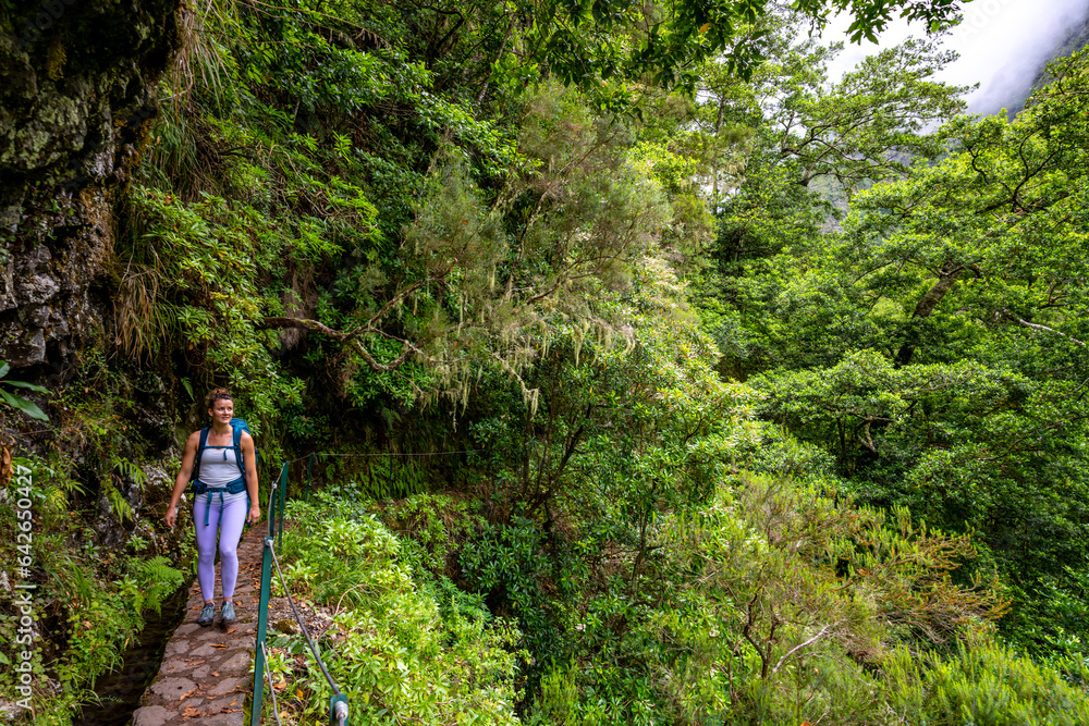 Backpacker tourist walks along picturesque hike trail overgrown by plants through Madeira rainforest. Levada of Caldeirão Verde, Madeira Island, Portugal, Europe.