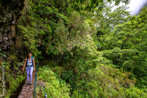Backpacker tourist walks along picturesque hike trail overgrown by plants through Madeira rainforest. Levada of Caldeirão Verde, Madeira Island, Portugal, Europe.
