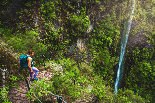 Female backpacker tourist enjoys view of overgrown waterfall while walking down a stair-like path in rainforest. Levada of Caldeirão Verde, Madeira Island, Portugal, Europe.