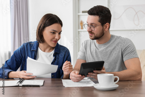 Young couple with papers discussing pension plan at wooden table indoors