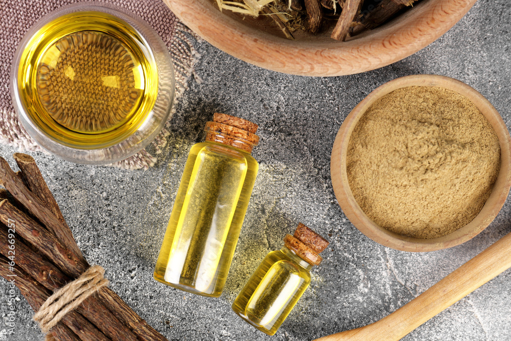Dried sticks of licorice roots, powder and essential oil on grey table, flat lay Dried sticks of licorice roots, powder and essential oil on grey table, flat lay