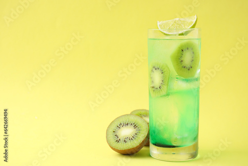 Glass of refreshing drink and cut kiwi on yellow background, space for text