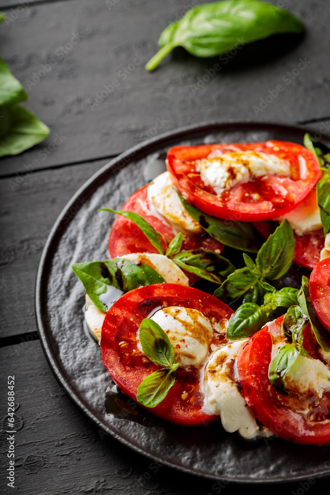 Delicious caprese salad with ripe tomatoes, mozzarella cheese and fresh basil leaves on dark wooden boards. Close up Delicious caprese salad with ripe tomatoes, mozzarella cheese and fresh basil leaves on dark wooden boards. Close up