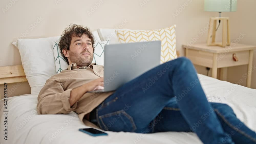 Young hispanic man using laptop lying on bed at bedroom Young hispanic man using laptop lying on bed at bedroom