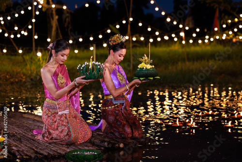 Obraz na płótnie Two thai woman holding a krathong sitting on a raft by the river, Asian women in