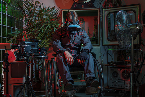 A man in overalls with a cyber helmet on his head, sitting in a wheelchair among old things, high technology and low standard of living of society, concept