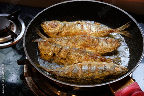 fried mackerel with turmeric spices in a black pan. seafood. ikan kembung goreng. photo