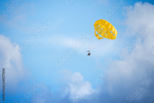 two tourists flying by parasailing with a yellow parachute, with blue sky and clouds in the background. Zona Hotelera (Hotel Zone), Cancun, Mexico