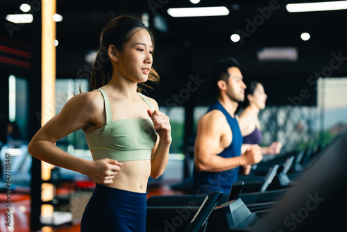 Fit young woman and man running on a treadmill during a workout class at fitness gym