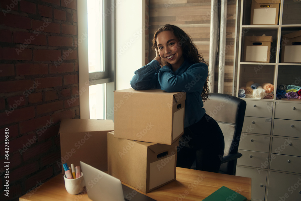 A young curly-haired logistics employee packs goods, collects parcels, puts things in a cardboard box, prepares a parcel for shipment, transports, sits on a windowsill and drinks a report in a book A young curly-haired logistics employee packs goods, collects parcels, puts things in a cardboard box, prepares a parcel for shipment, transports, sits on a windowsill and drinks a report in a book