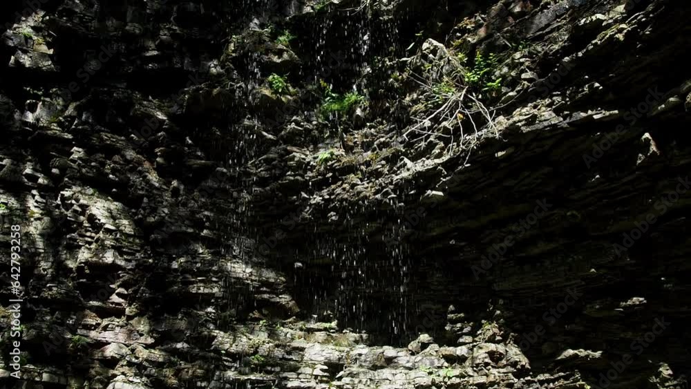 View of falling water from a cliff in the forest. Bottom-up view of a rock with a small waterfall formed by a stream. A small waterfall with crystal cold water in the Carpathians, Ukraine.