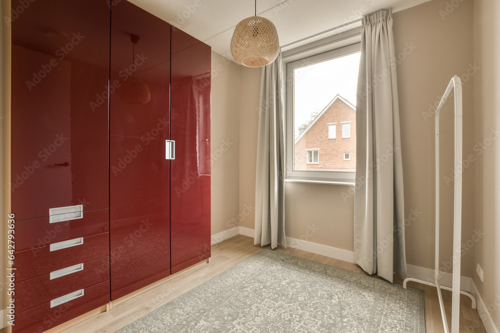 a bedroom with red cupboards and white curtains on the window sies, in front of an open door a bedroom with red cupboards and white curtains on the window sies, in front of an open door