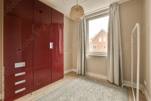 a bedroom with red cupboards and white curtains on the window sies, in front of an open door