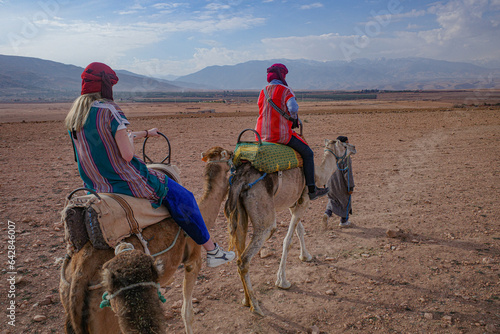Marrakech, Morocco - Feb 22, 2023: Tourists ride Dromedary camels through the Agafay desert