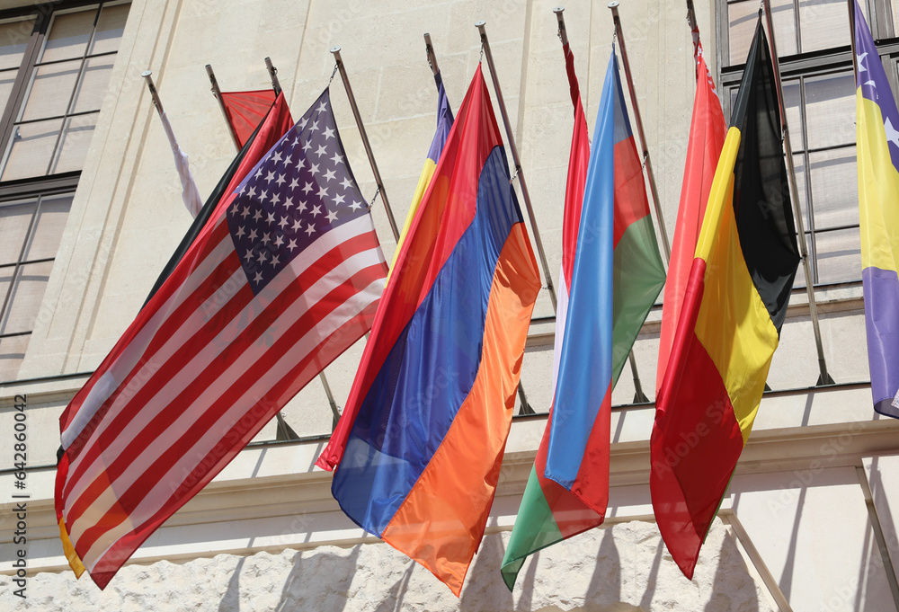 lots of colorful flags of various world nations and american flag hanging outside government building