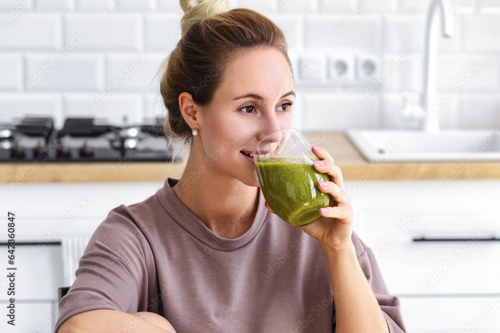 Happy young woman drinking green diet smoothie in the kitchen of her home for health, healthy lifestyle concept Happy young woman drinking green diet smoothie in the kitchen of her home for health, healthy lifestyle concept