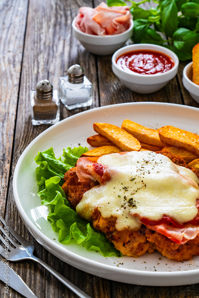 Milanesa Napolitana - fried breaded cutlet with ham, mozzarella cheese and tomato sauce on wooden background
