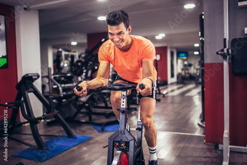 Man biking in the gym, exercising legs doing cardio workout cycling bikes. © Mediteraneo