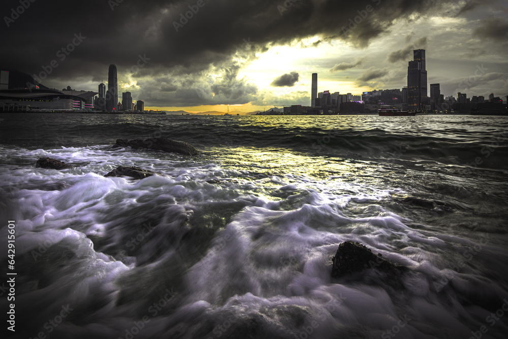 hong kong city skyline at sunset with sea wave in foreground