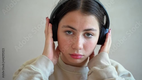 Young teen girl woman with headphones looking at camera upset disappointed sad listen to music radio podcast sorrow pubertal life. Technology in daily life, age difficulties photo