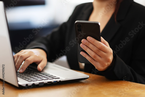 Businesswoman in working environment typing on a laptop and holding smartphone