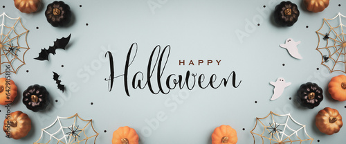 Halloween holiday background with party decorations from  pumpkins, bats, ghosts, spider webs on blue top view. Greeting card with text inscription Happy Halloween in banner format..