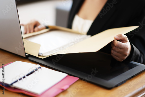 Businesswoman in working environment with  a laptop and reading papers