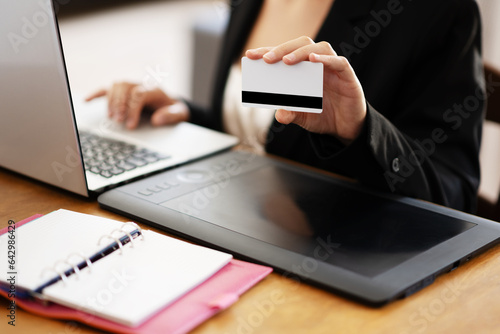 Businesswoman in working environment typing on a laptop and holding card