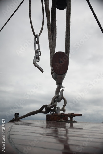 The hook of a ship's winch hangs above the wooden deck of a sailing ship