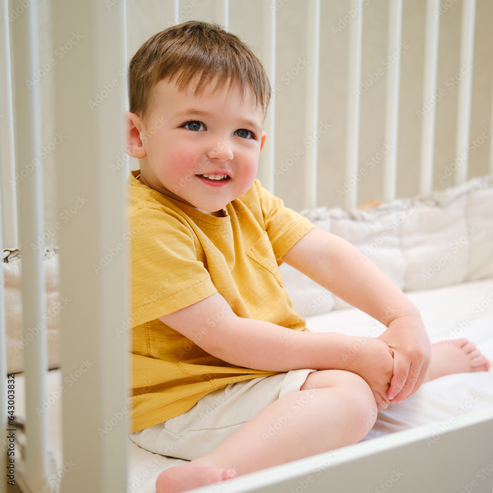 Portrait of a toddler baby sitting in a white crib. Kid aged about two years (one year eleven months)d Portrait of a toddler baby sitting in a white crib. Kid aged about two years (one year eleven months)d