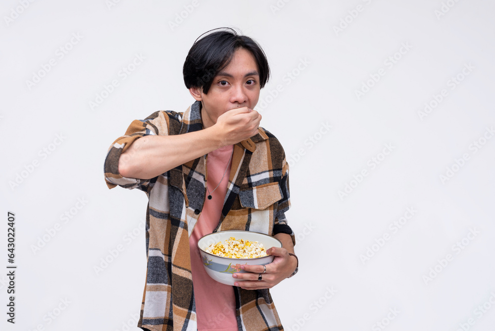 A young asian man gorging on popcorn while watching a movie. Isolated on a white background.