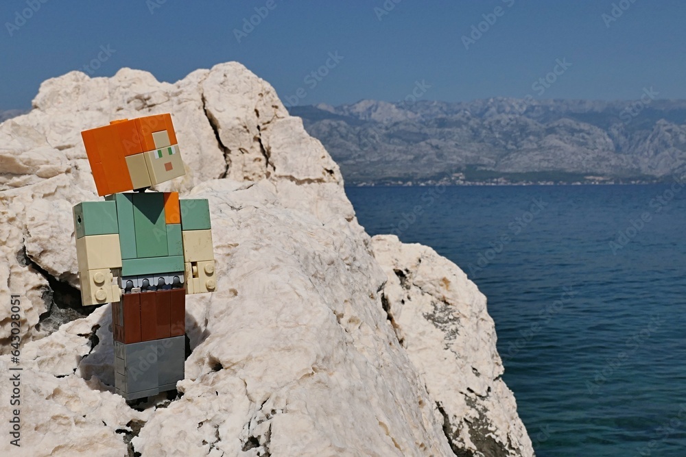 Obraz premium LEGO Minecraft action figure of main female character Alex standing on rocky beach of Radanovac in northern Dalmatia, near town of Razanac. Velebit mountain in background.