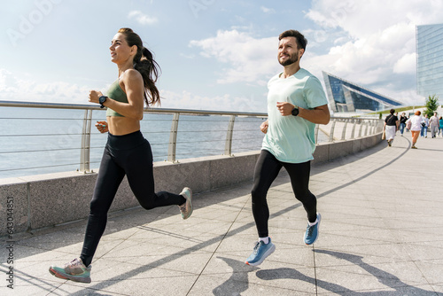 People in sportswear together runners, physical education and sports. Running man and woman train.  Using smart watches and a fitness app.  Team exercises of a young couple.