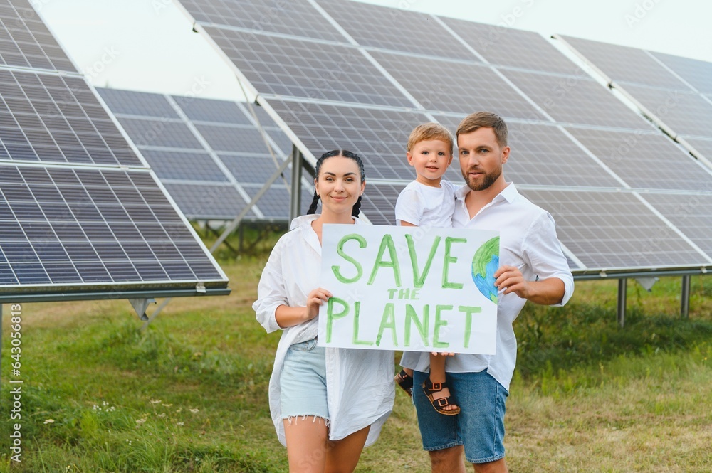 A family of activists and nature defenders stands with a poster about the protection of nature against the background of solar panels. The concept of green energy and nature protection.