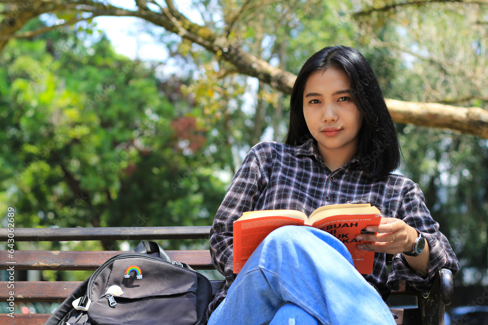 happy young asian woman college student with smiling face enjoy read a book for exam in the park