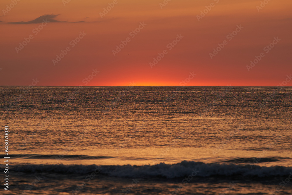 The glowing sun sinking on the horizon of the sea or ocean