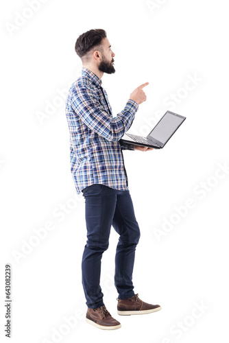 Young adult stylish business man with laptop pointing finger at presentation looks up. Full body isolated on transparent background.