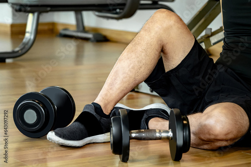 Fotografia Male athlete massaging his wrist and hand suffering from wrist pain caused by sprain or joint fracture from overweight dumbbell lifting in fitness gym