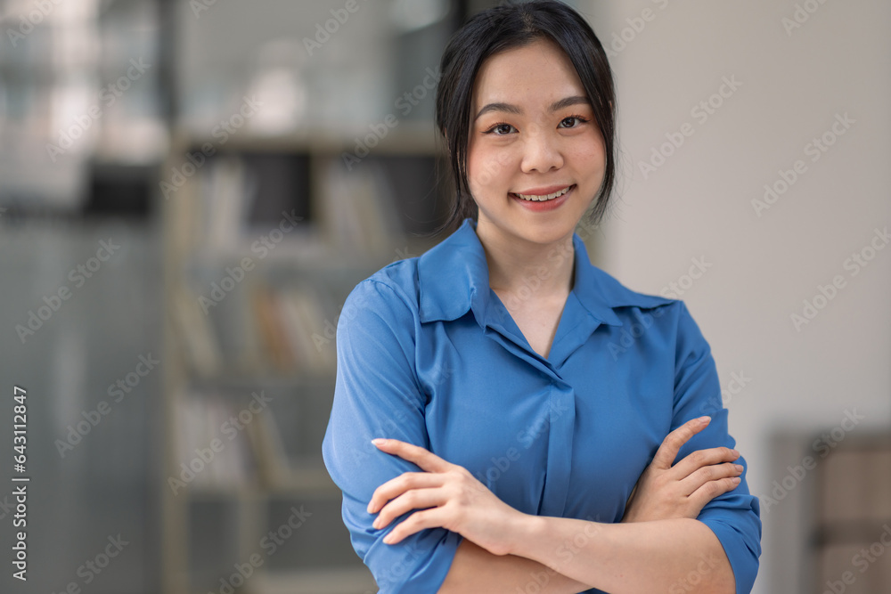 Portrait of happy asian woman smiling, posing confident, cross arms on chest, standing against office background Portrait of happy asian woman smiling, posing confident, cross arms on chest, standing against office background