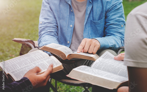 Christian life bible study concept Group of Christian friends sitting together studying the Bible Outdoors in the park and pray together and live according to God\'s word