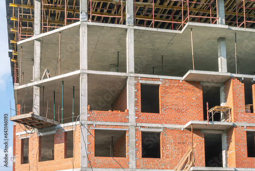 Installation of partitions and exterior walls made of red brick. The frame of a building under construction. Reinforced concrete frame of the house. Scaffolding in the construction of buildings