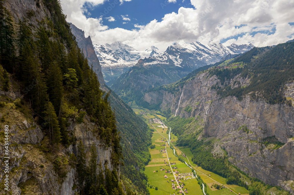 Fototapeta premium Aerial Drone View of The Swiss Alps with Buildings Sitting Along the Hills and Snow Covered Mountains in the background in Switzerland in Summer