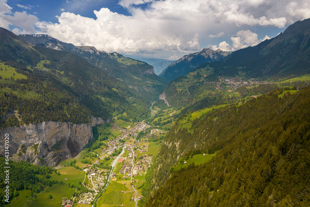 Aerial Drone View of The Swiss Alps with Buildings Sitting Along the Hills and Snow Covered Mountains in the background in Switzerland in Summer